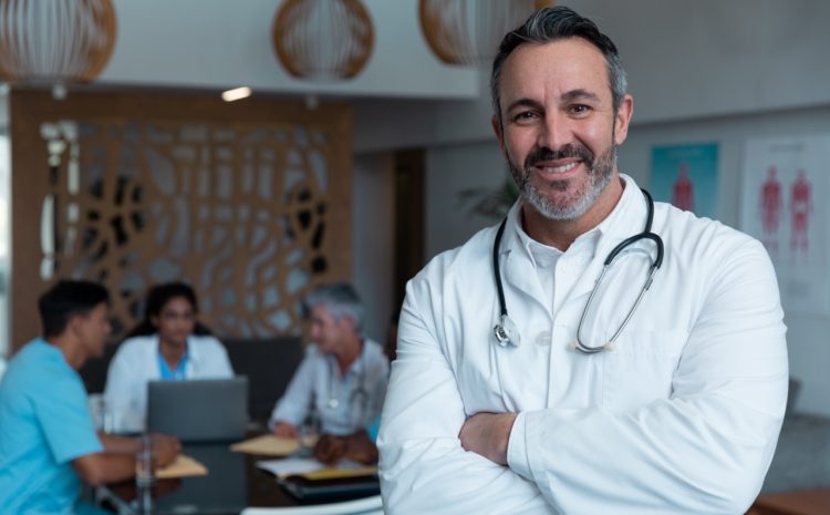 Portrait of smiling caucasian male doctor, with colleagues in discussion in the background. medicine, health and healthcare services.